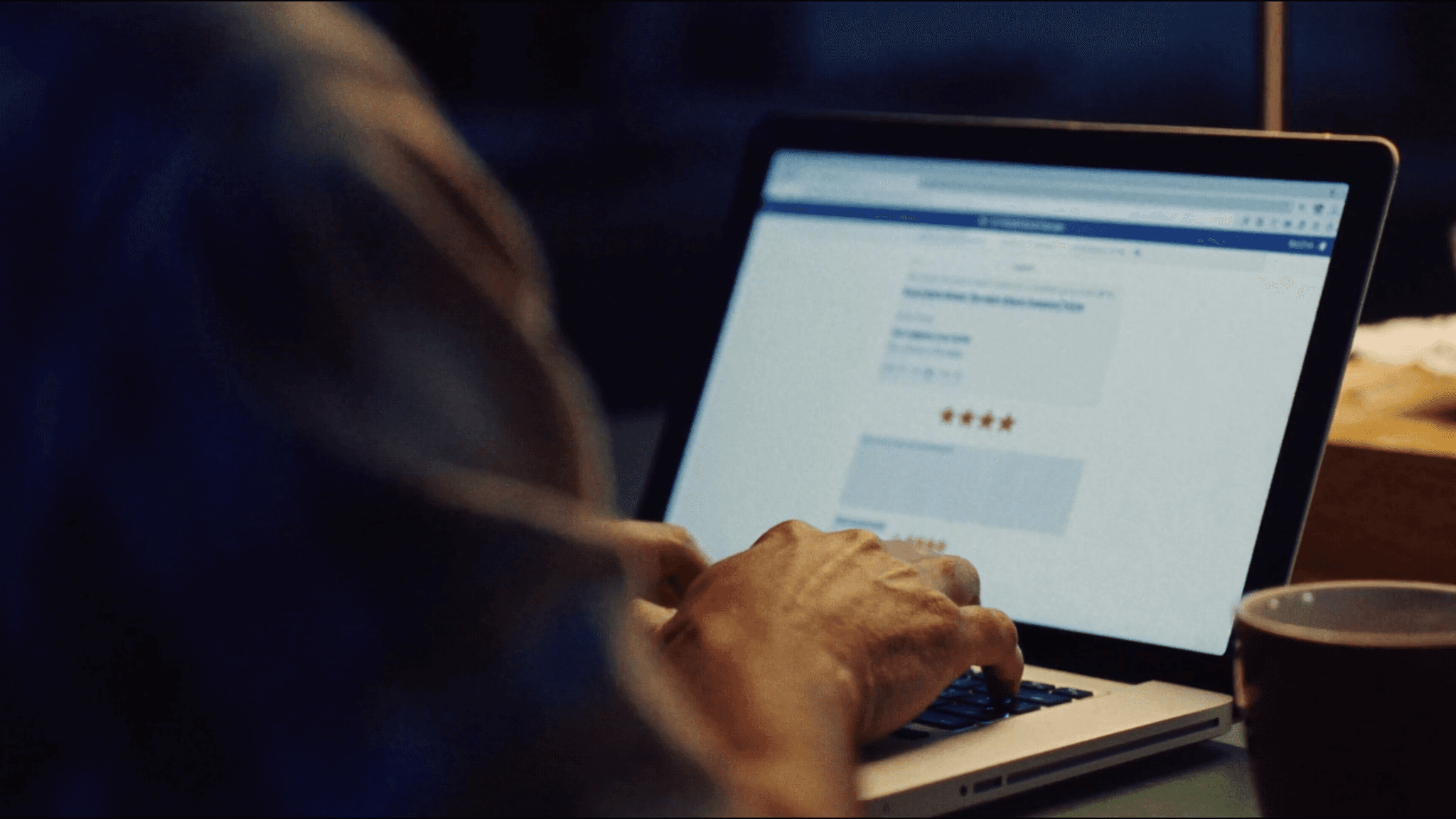 A contractor at a kitchen table at dusk, calmly typing a reply to a one-star review on a laptop
