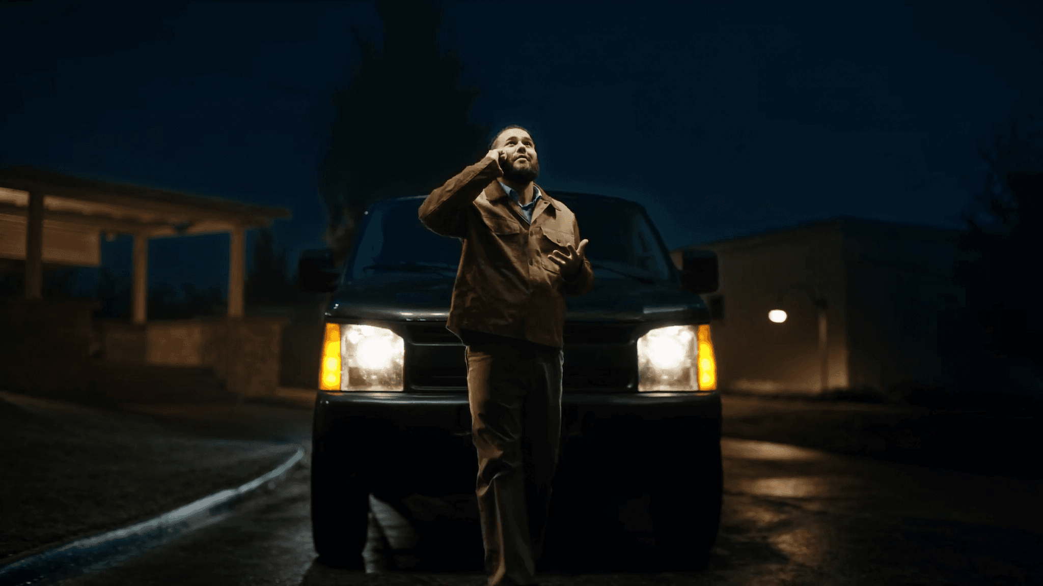 A home-services contractor answering an emergency call at night in a driveway, service van headlights glowing on wet pavement